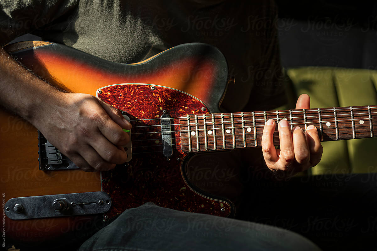 Close up on the hands of a man playing an electric red guitar