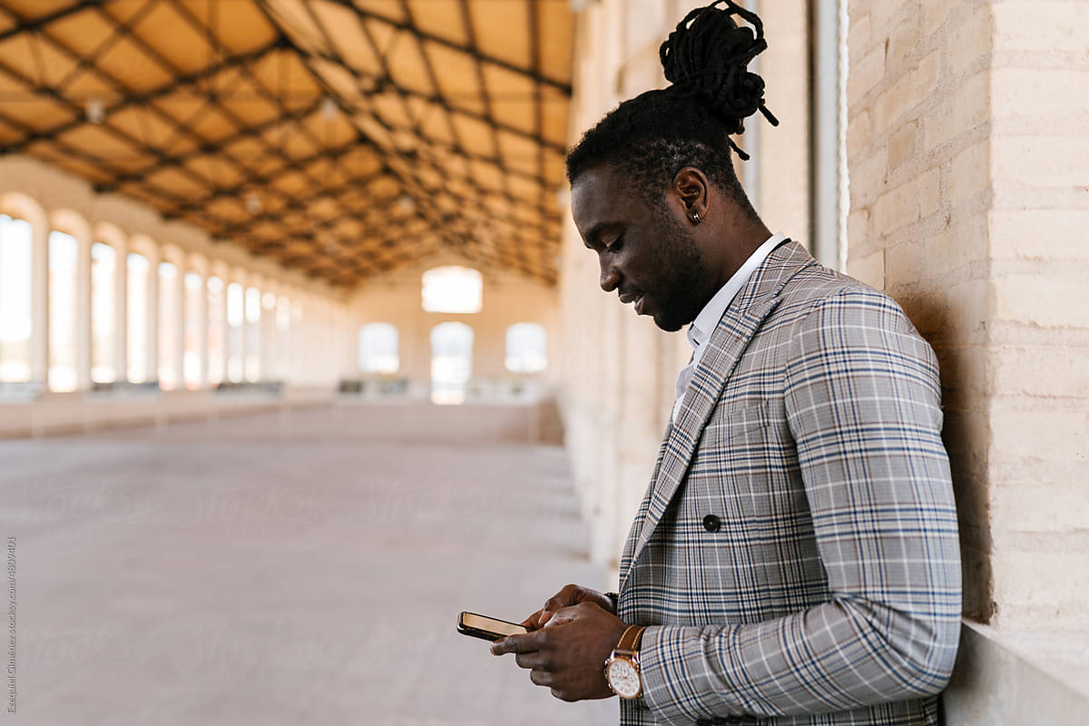 Stylish black man using smartphone in spacious building