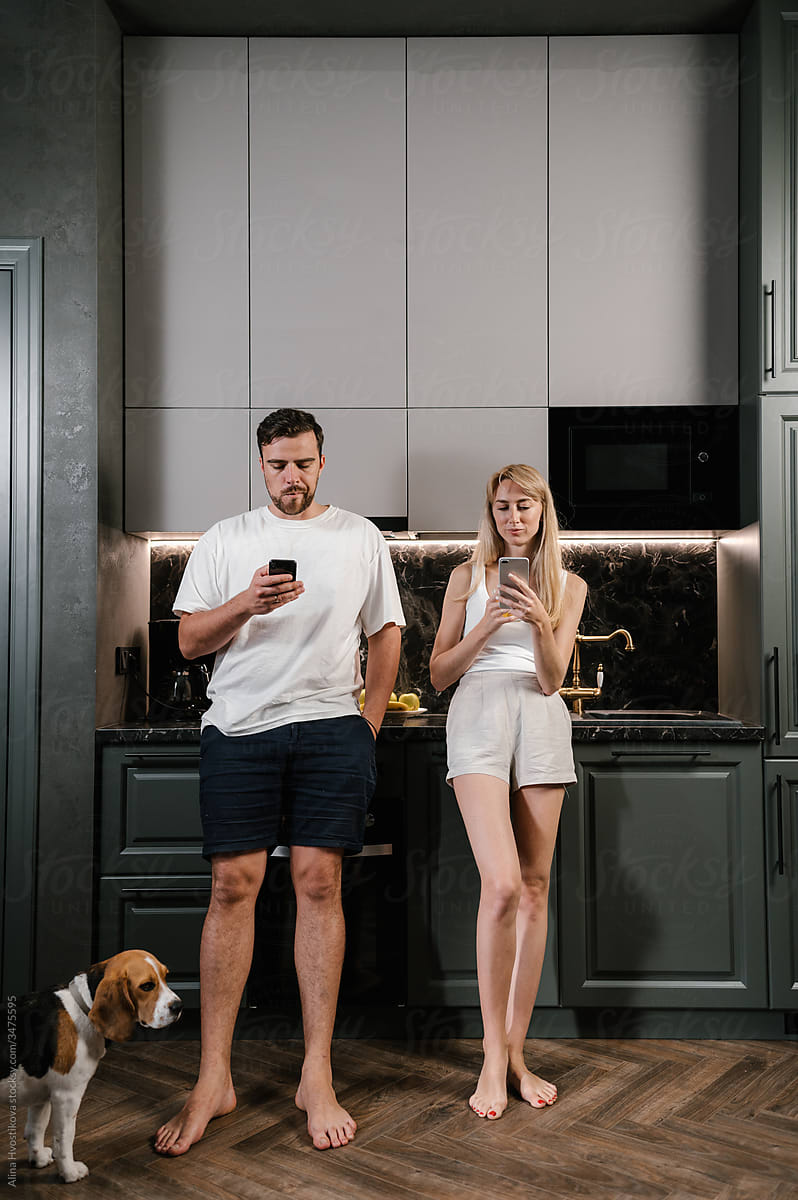 Couple using smartphones near dog in kitchen