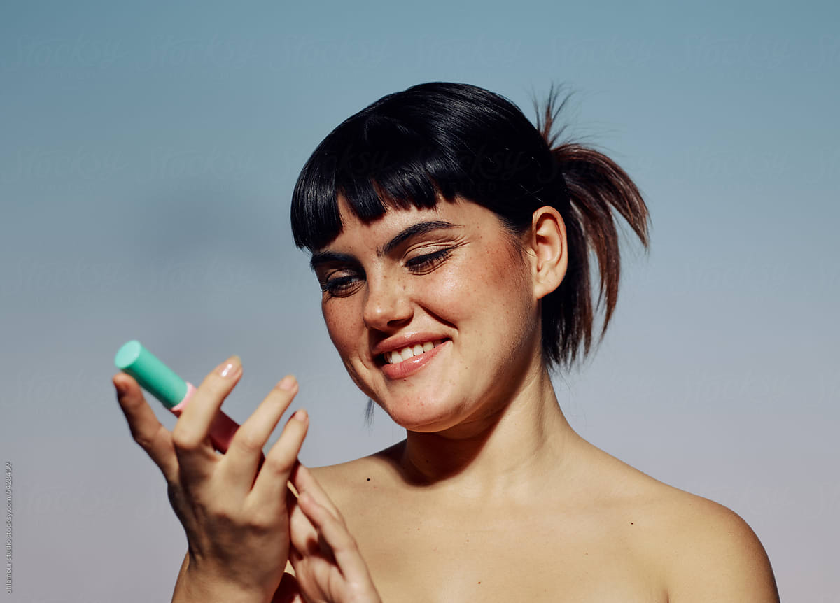 Happy woman looking at make up product, a facial highlighter