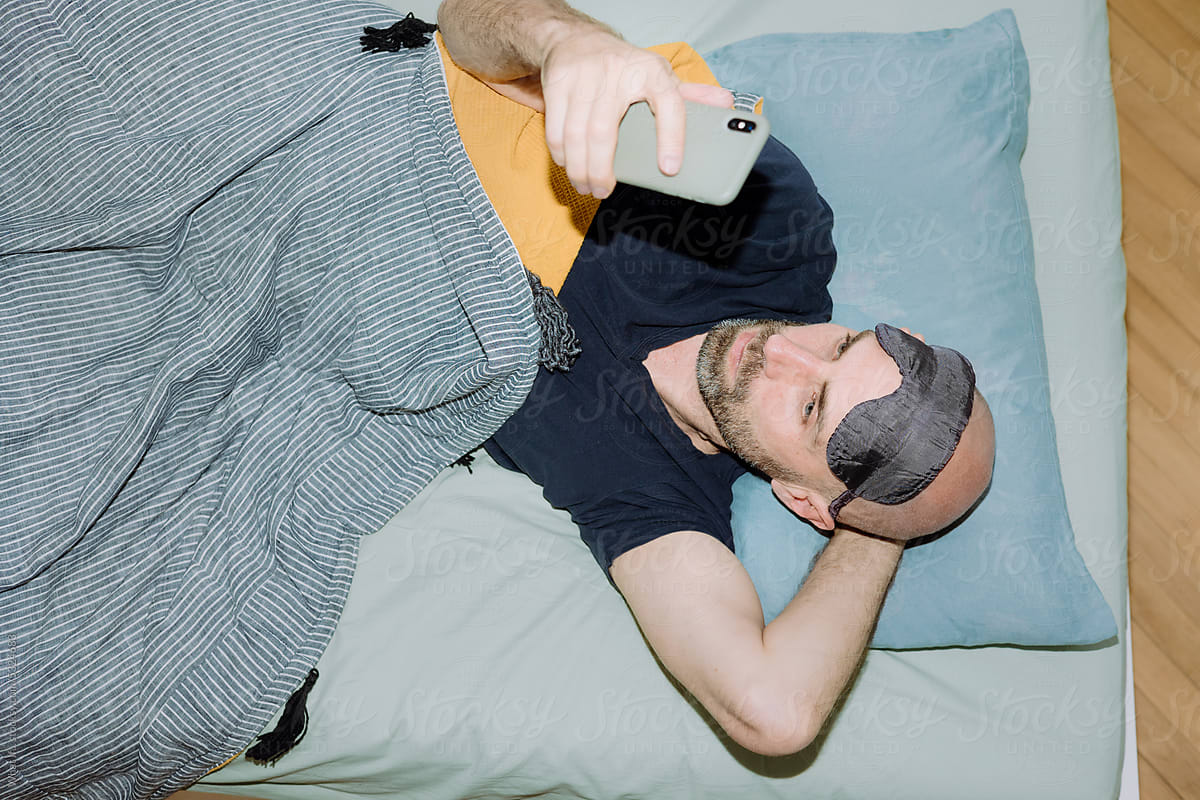 Top view man with stubble using his phone in bed.