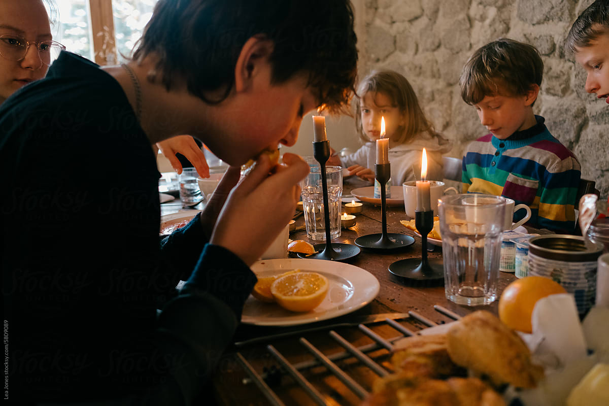 teen boy eating orange during family breakfast/brunch