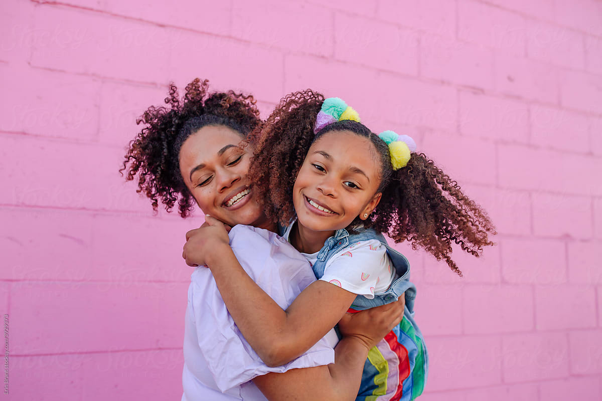 Girl hugging pretty mom in front of pink wall