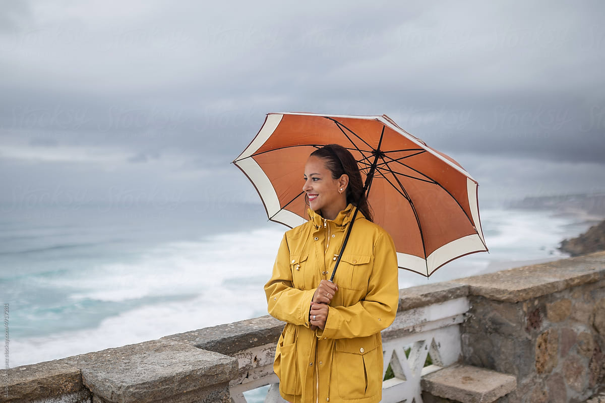 young woman with umbrella and yellow raincoat walking by the sea