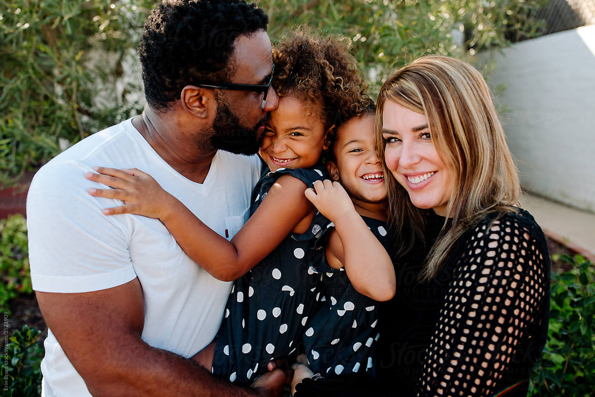 Affectionate parents holding sweet biracial daughters in matching outfits