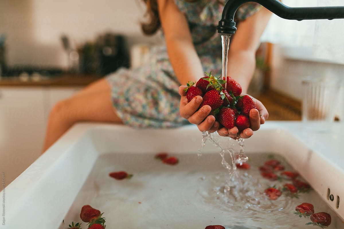 Girl holding strawberries and washing them.