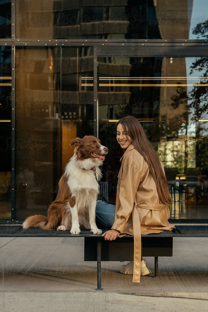 Happy woman with Border Collie dog sitting on bench in street