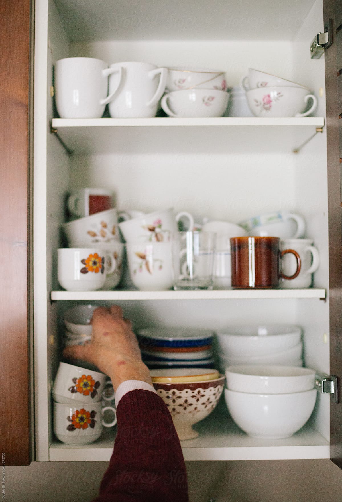 Senior woman taking cups from a shelf in the kitchen