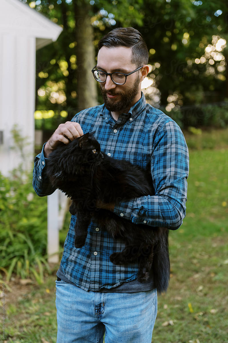 Young smiling man holding his black cat outdoors