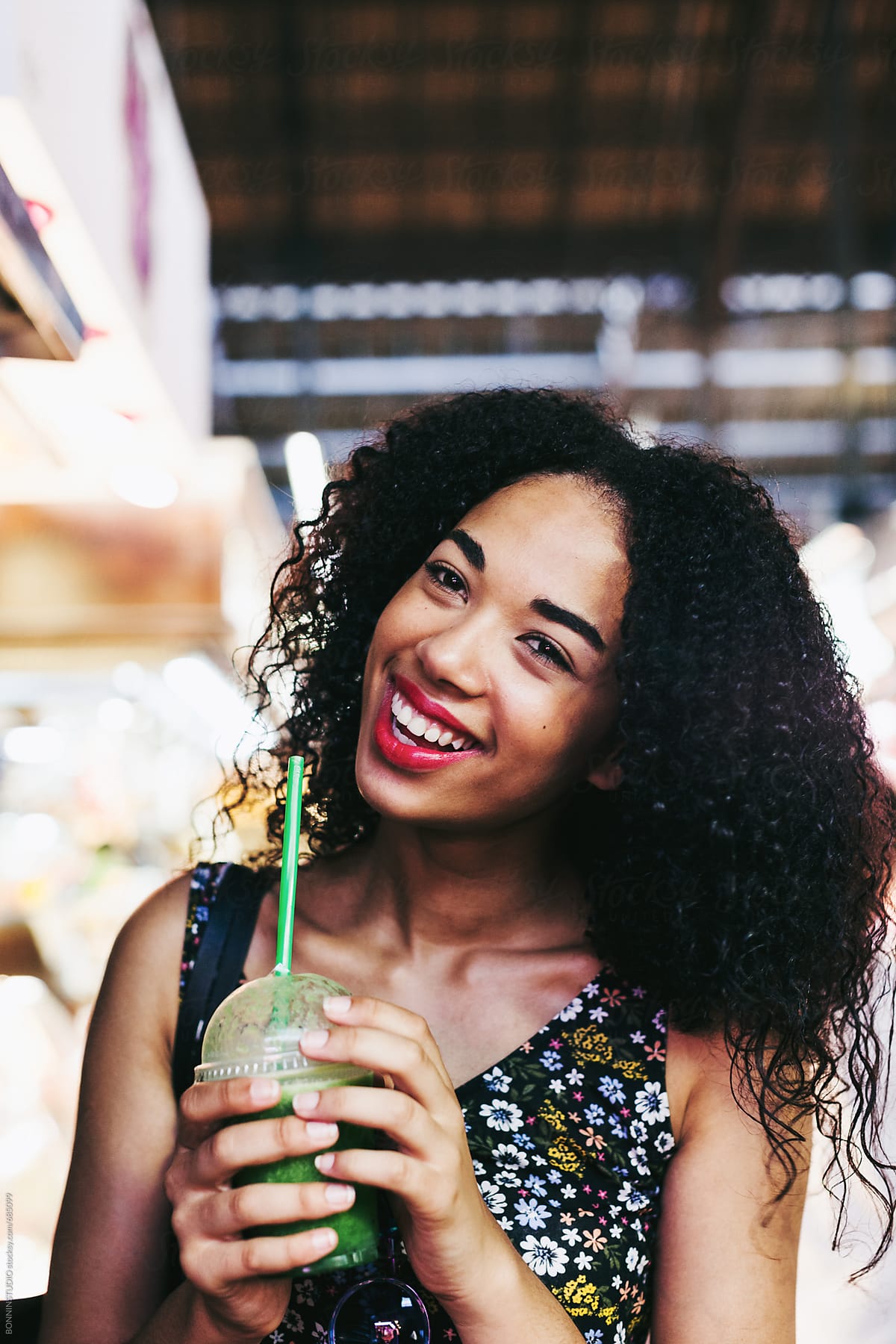 Portrait of a happy latin woman holding a fresh smoothie standing on a marketplace.