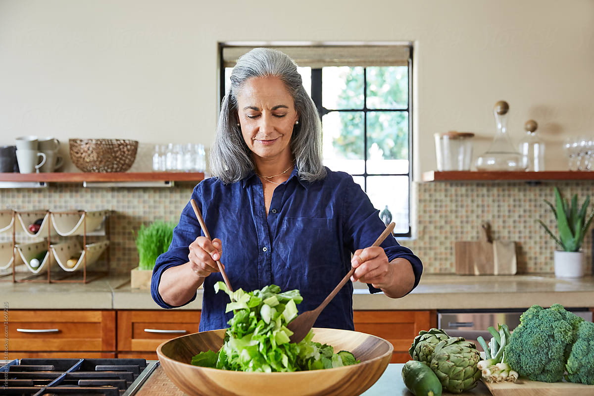 Mature Woman Tossing A Healthy Salad In The Kitchen At Home By Stocksy Contributor Trinette