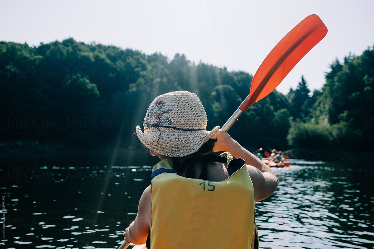 back of woman on a kayak wearing a  straw hat.