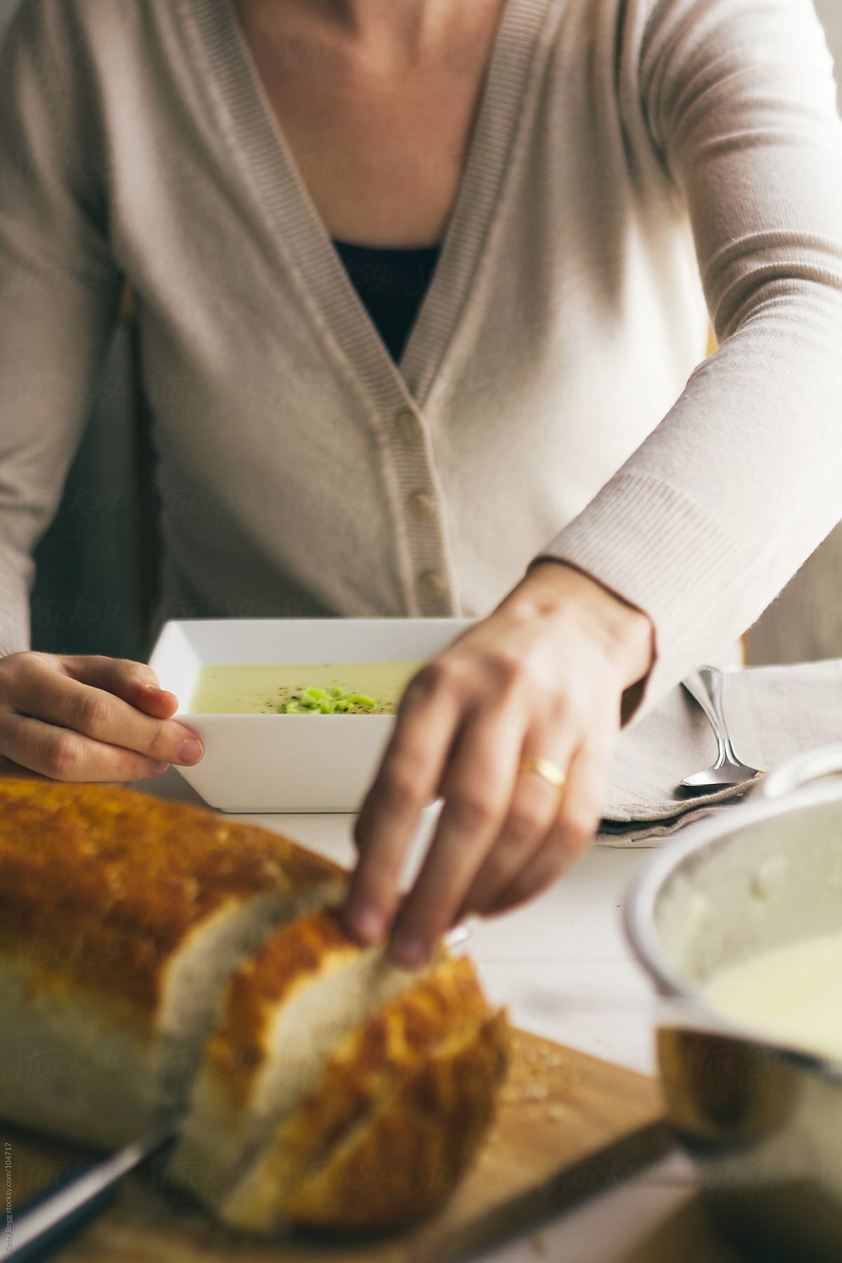 Woman reaching for bread with soup bowl set in front of her