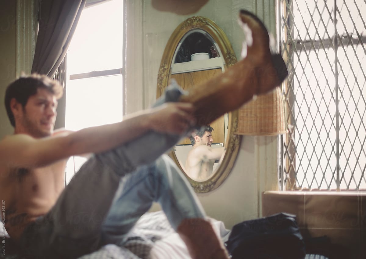 Shirtless Man in Jeans Struggling to Put Boots on in Bed