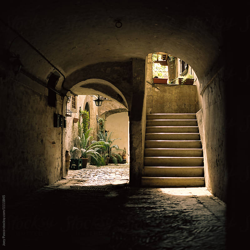 Shadowy passageway leads to stairs and small courtyard in Italy