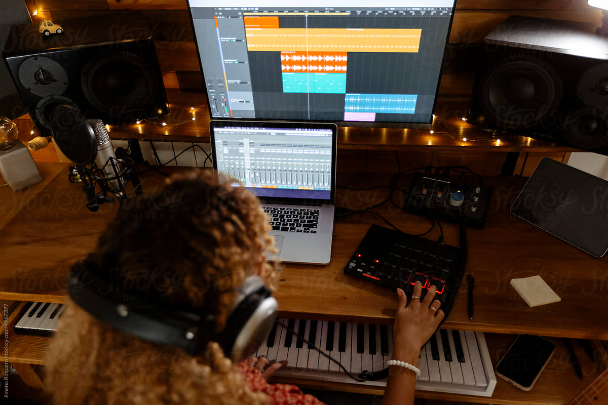 Music producer at home studio using keyboard controller from behind