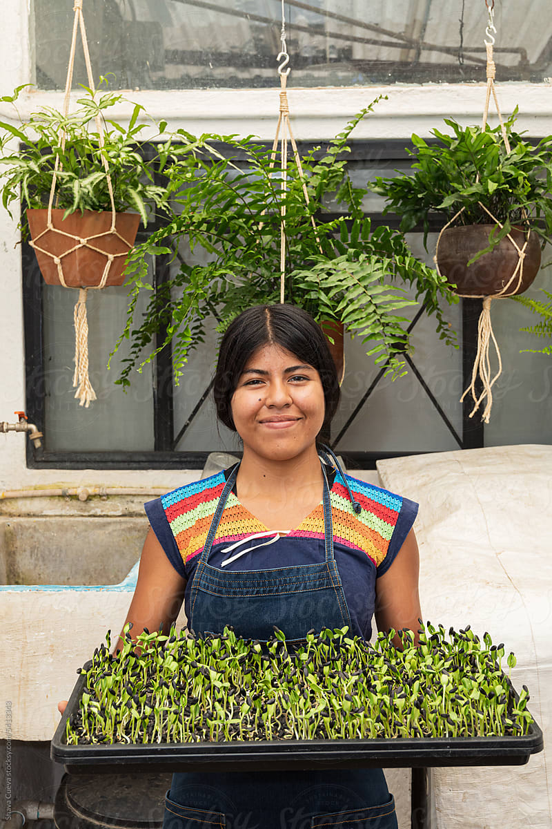 A happy woman holding a tray of sunflower microgreens sprouts