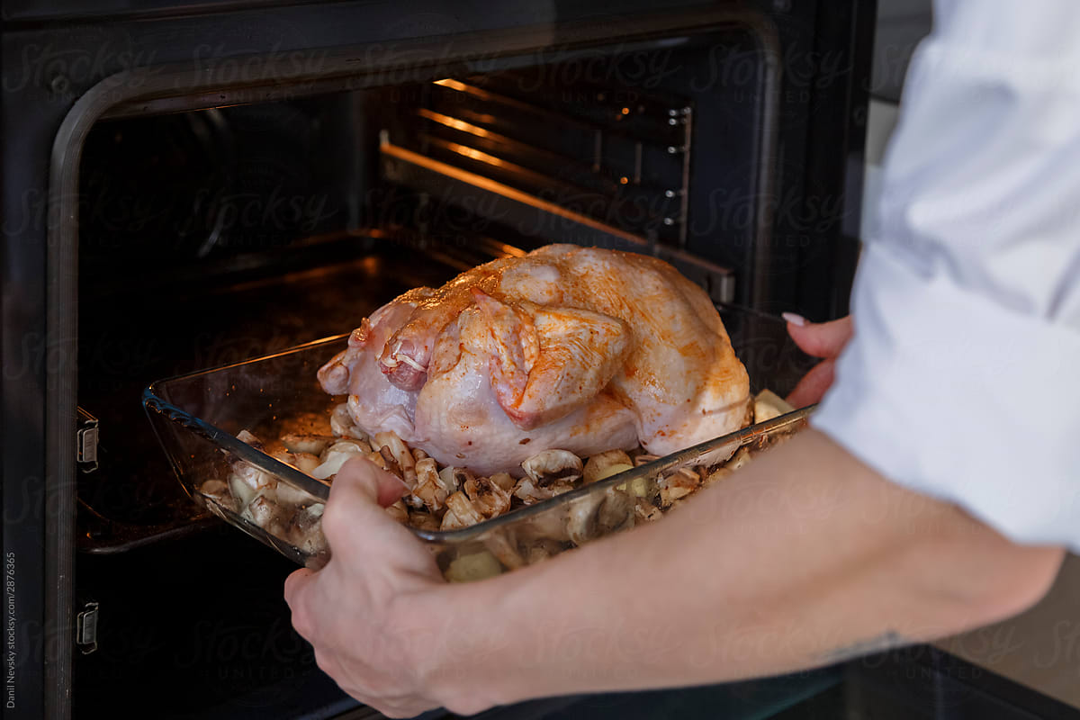 Cook diligently putting spiced poultry with vegetables in to oven