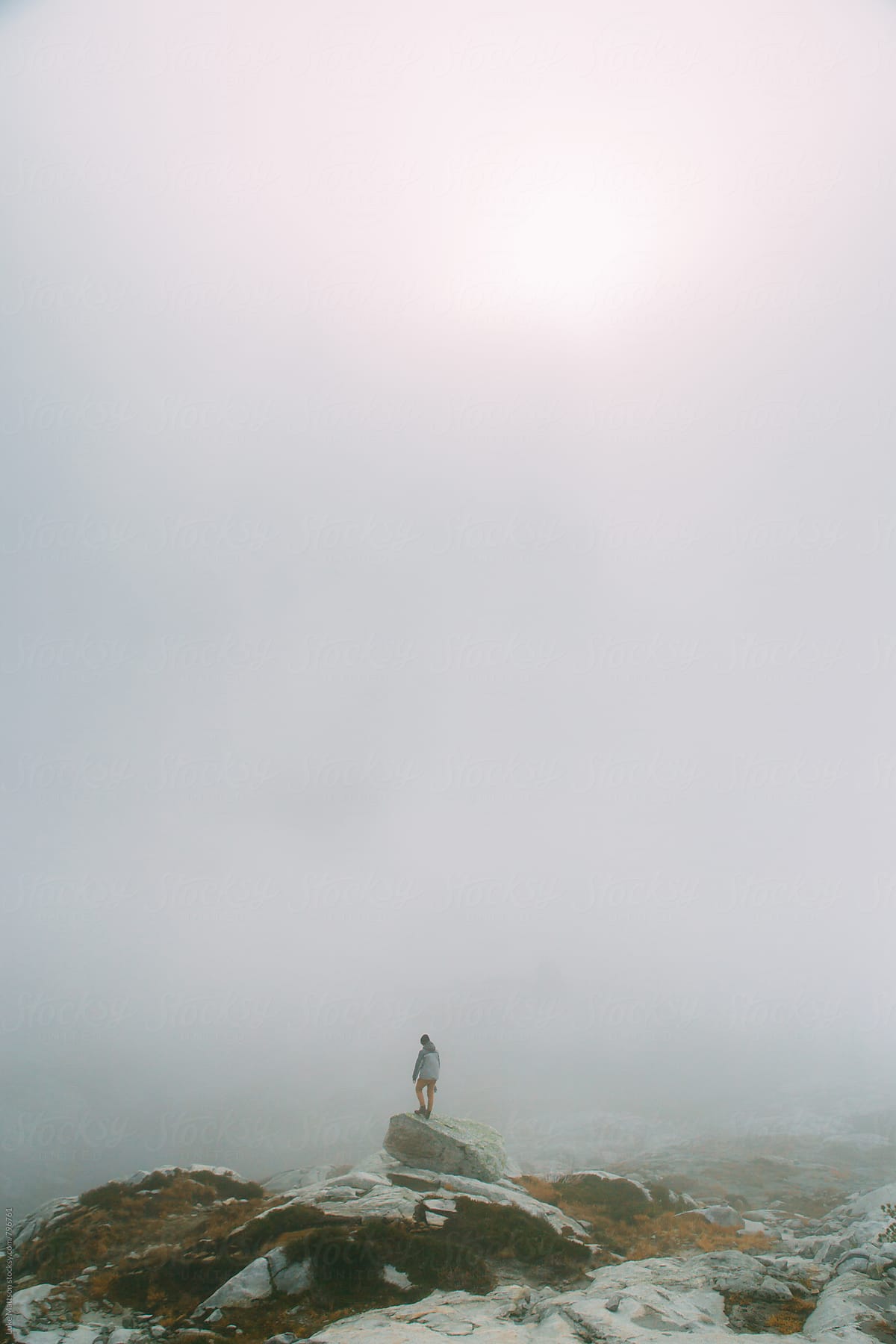 Man Standing Alone On Granite Boulder In Thick Fog