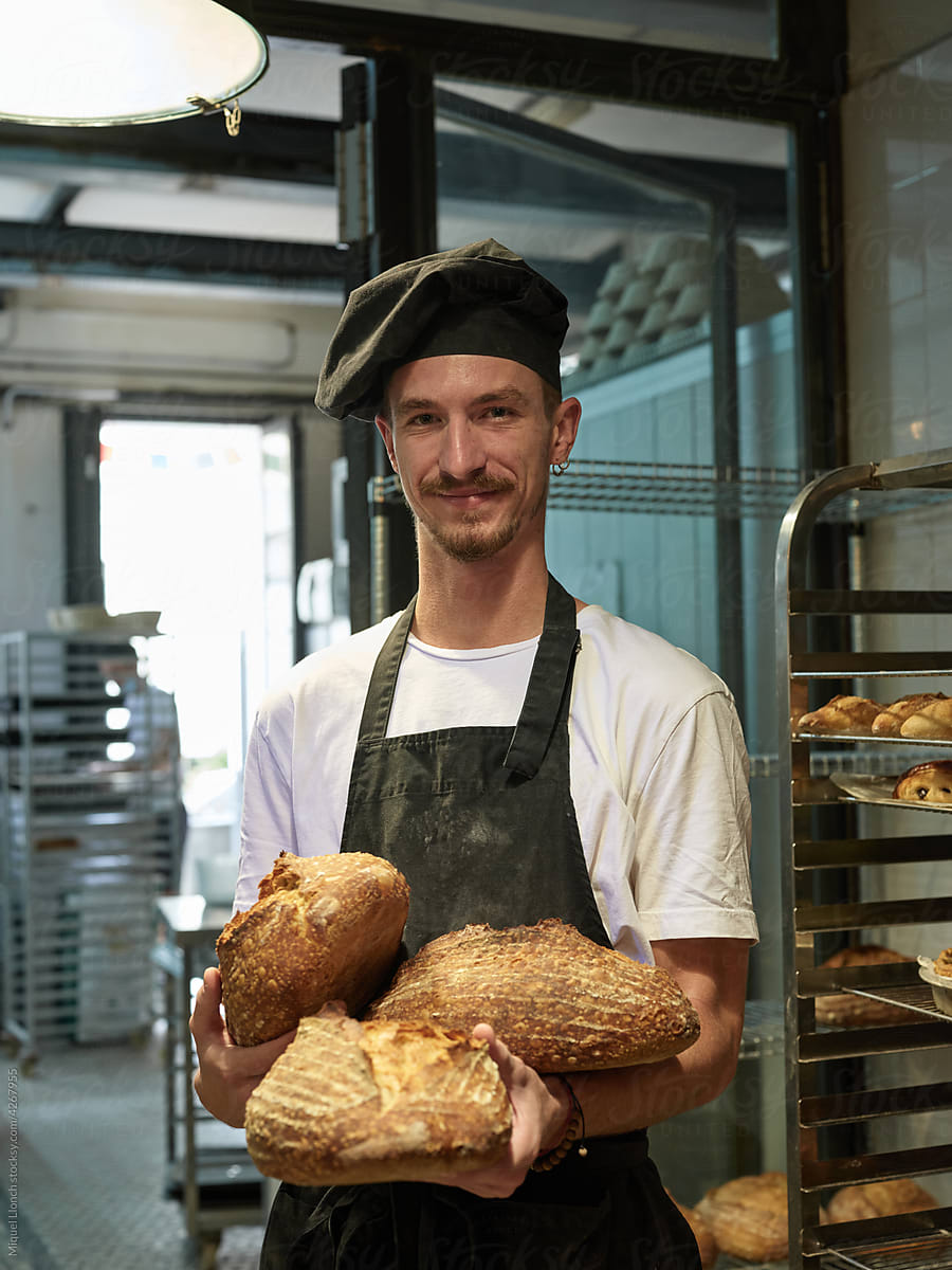 Artisan baker holding loafs of bread in the shop