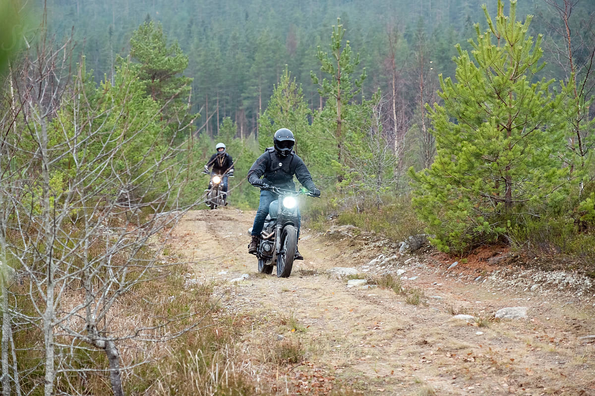 Two riders on classic motorcycles climb a dirt road