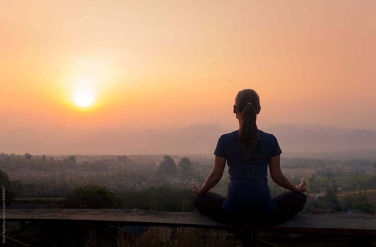 Woman meditating with view of rising sun over the mountains