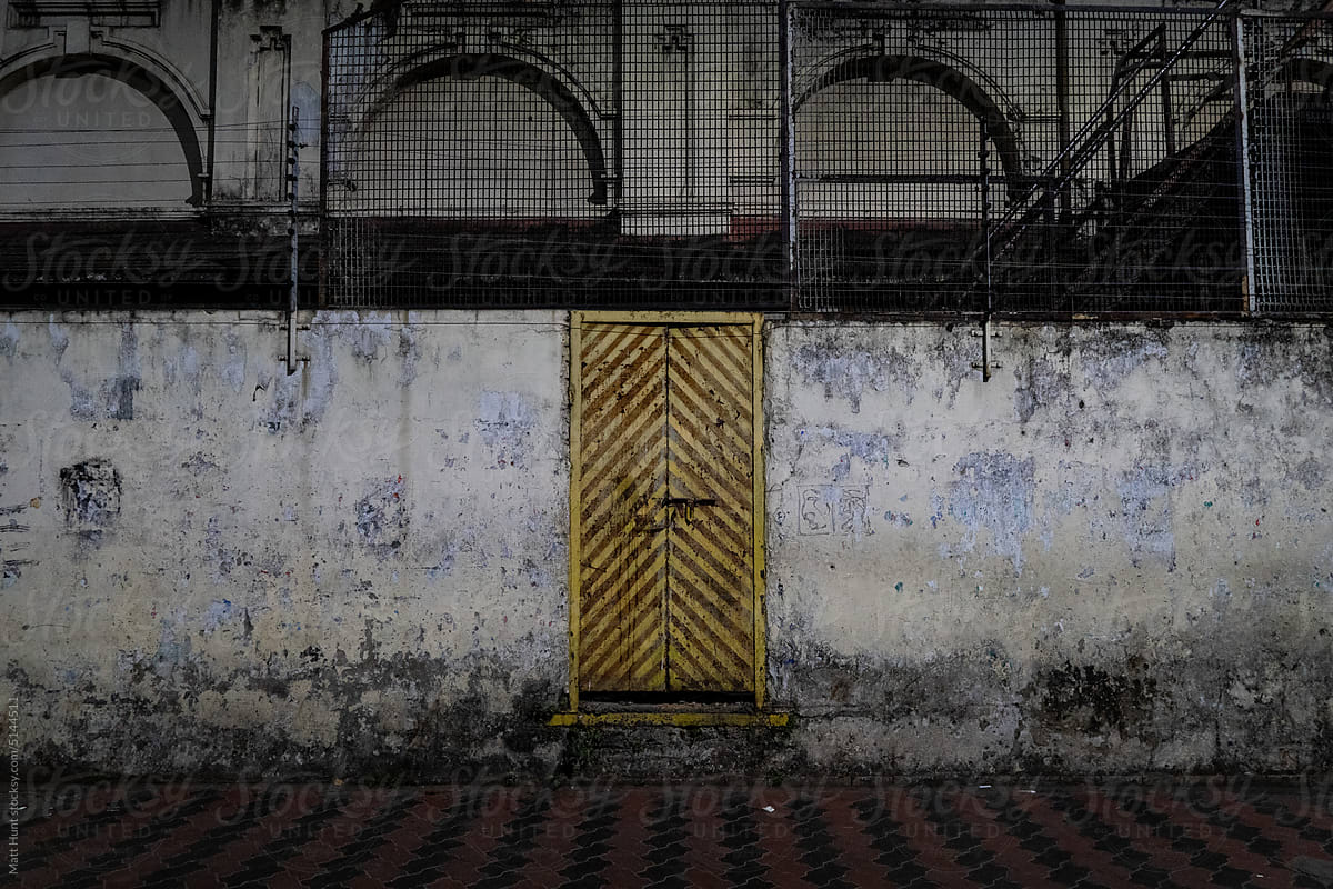 A yellow door in the middle of a rustic concrete wall in Kolkata