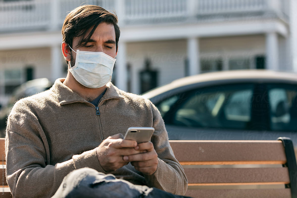 Virus: Man Wearing Medical Mask Uses Phone While Sitting On Benc
