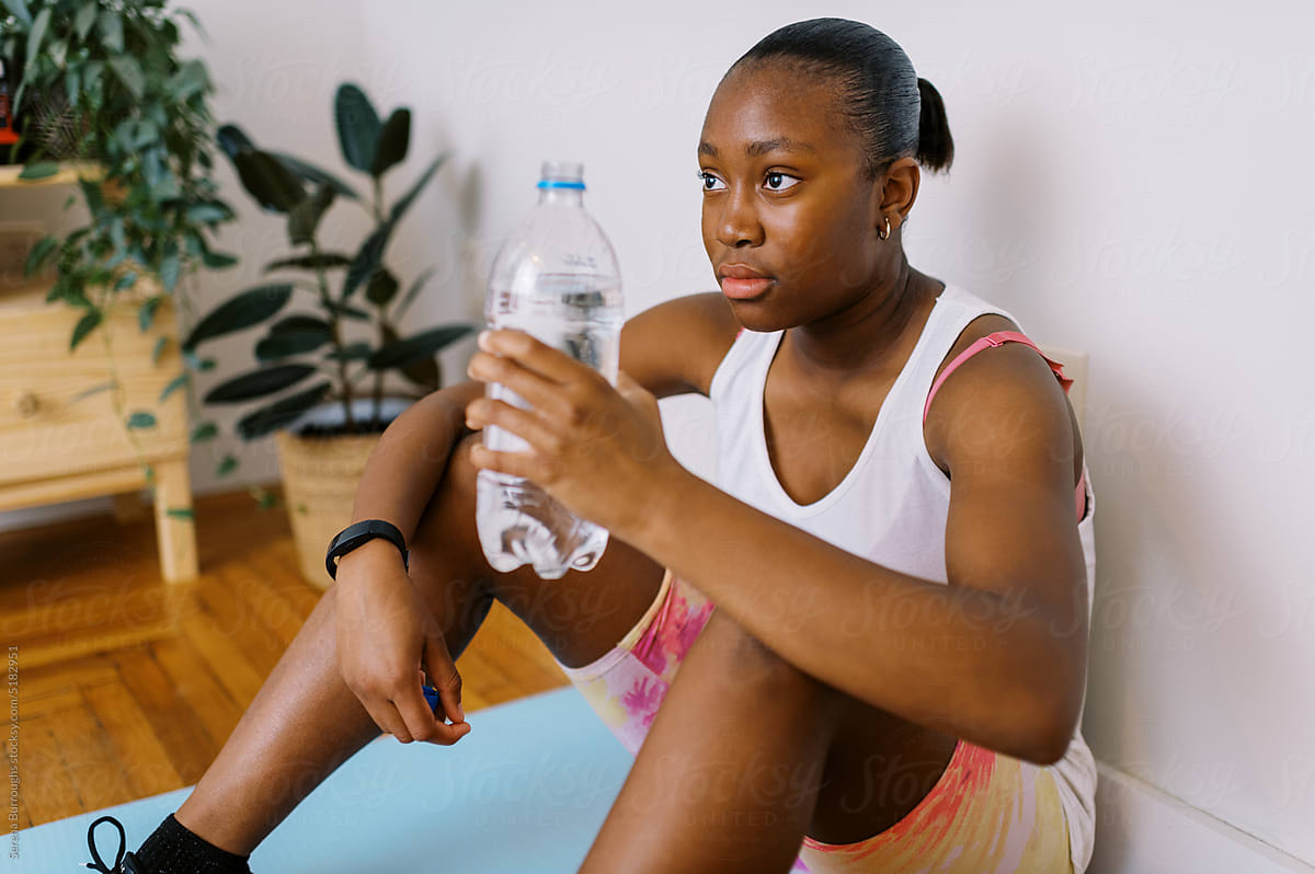 fit black tween girl drinking water from bottle after work out indoors