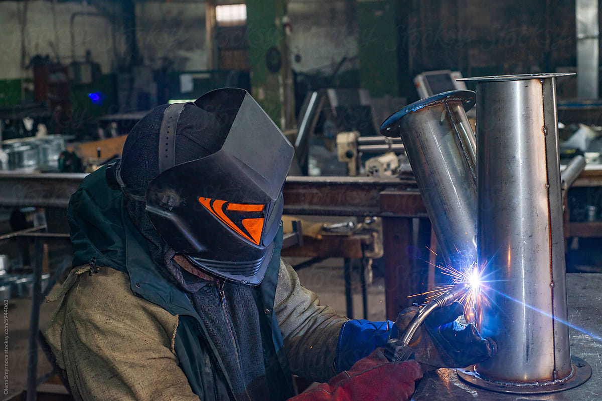 Male welder is welding stainless pipe in industrial workshop