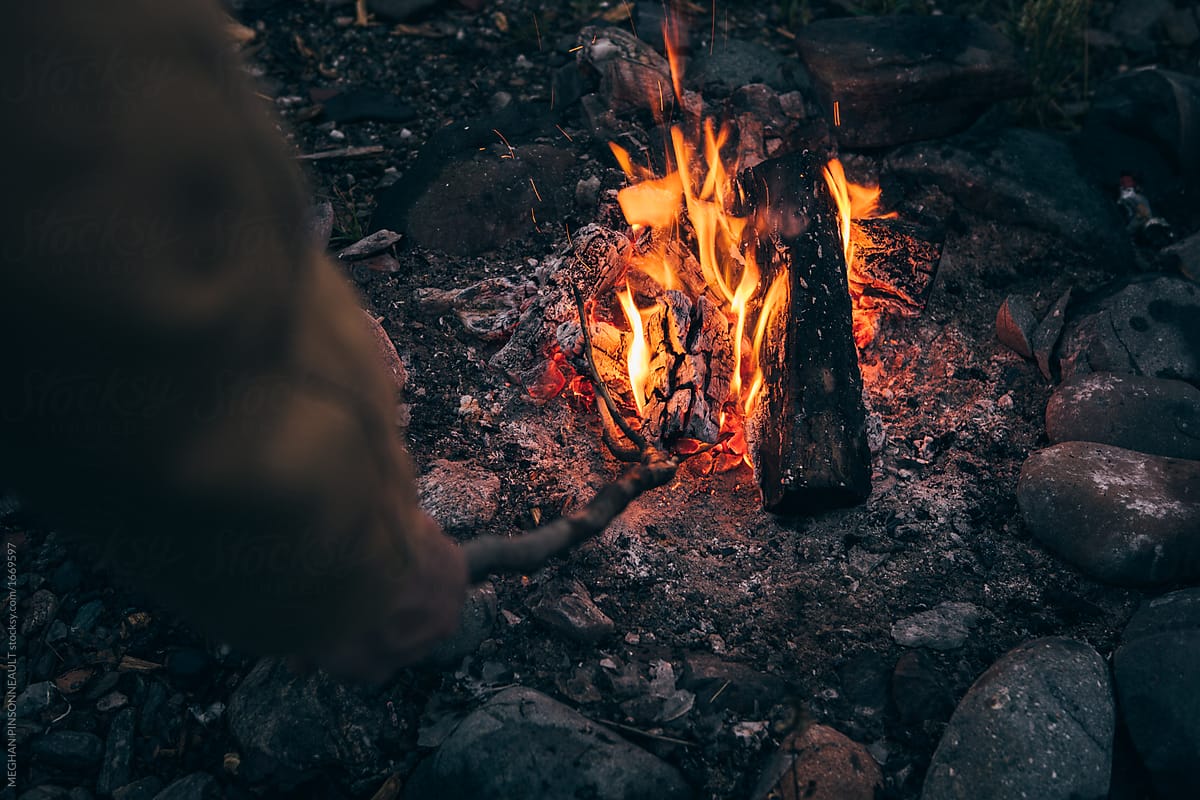 Man Poking Campfire at Dusk in Alaska