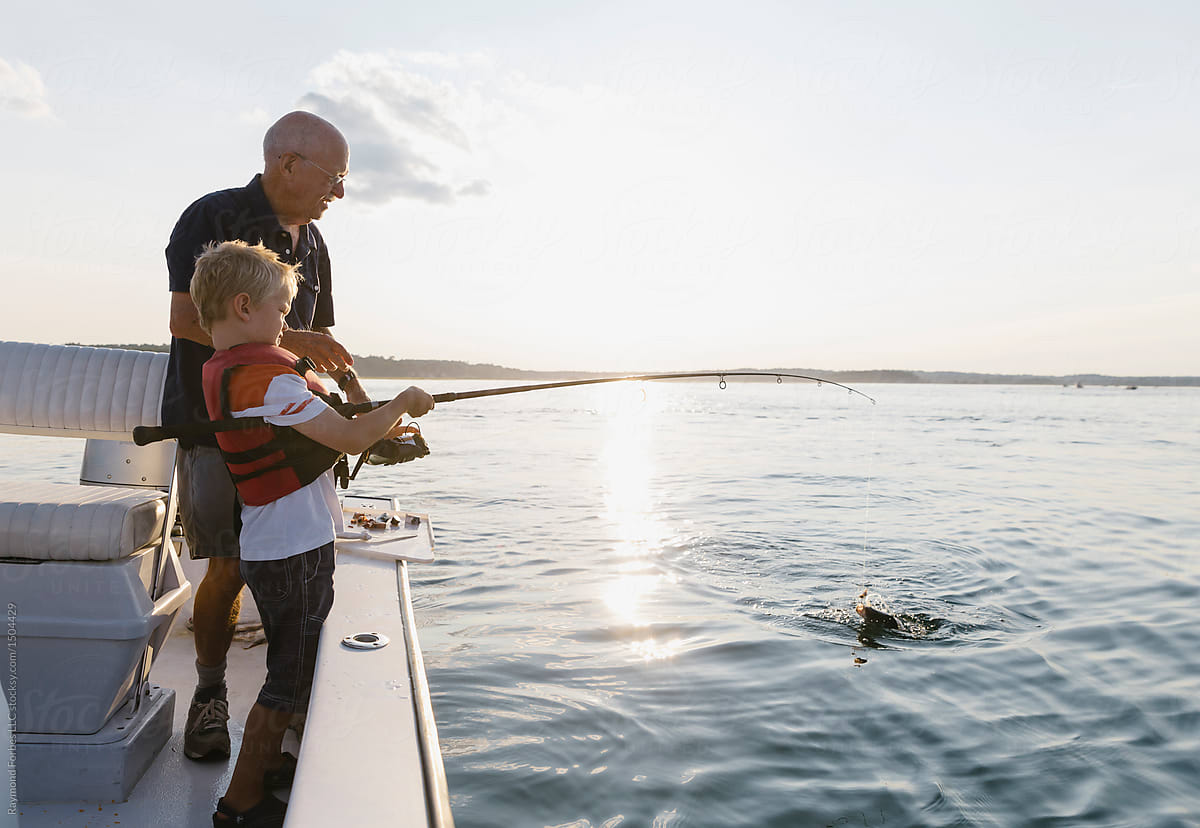Grandfather fishing with grandson on boat and boy reels in fish