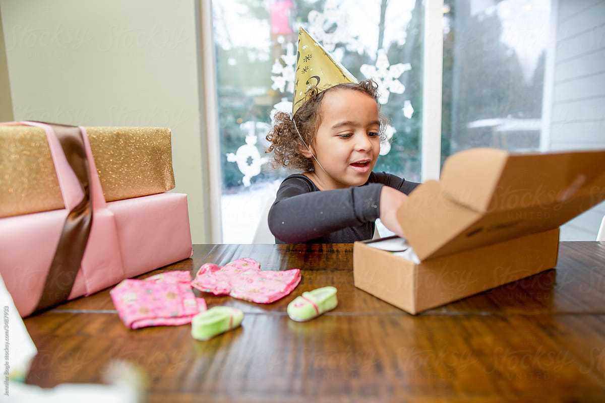 Excited girl in party hat opens presents at a table