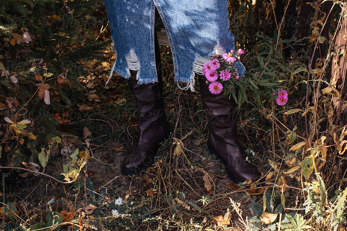 Crop florist in jeans and leather boots with flowers