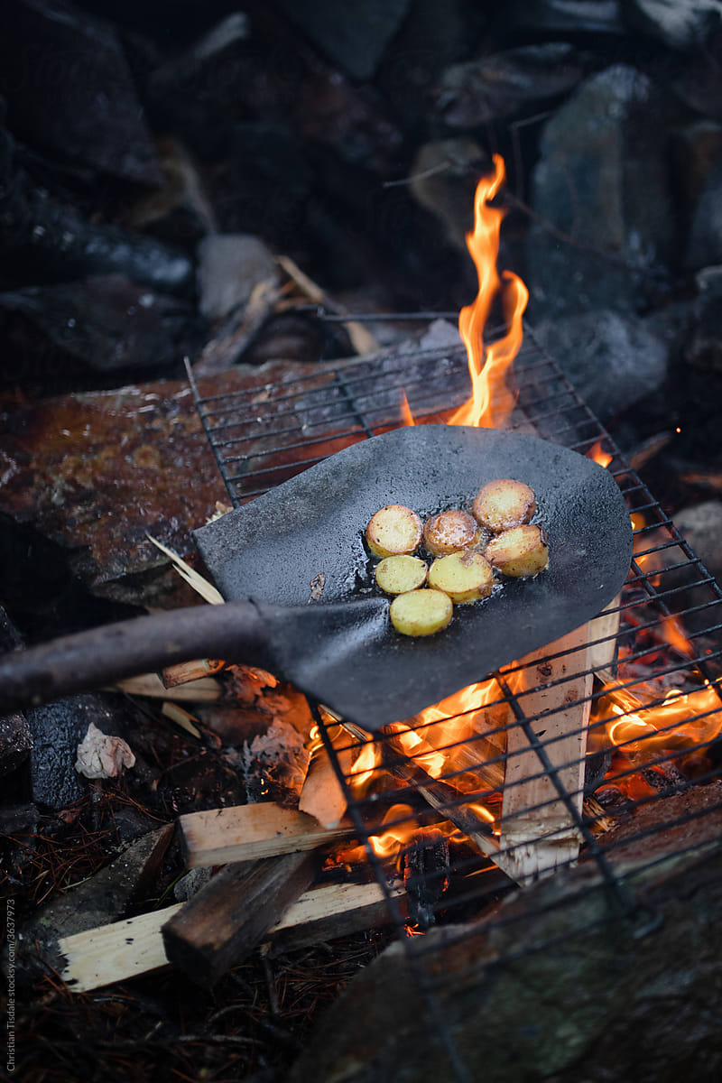 Potatoes being cooked over an open fire in a shovel