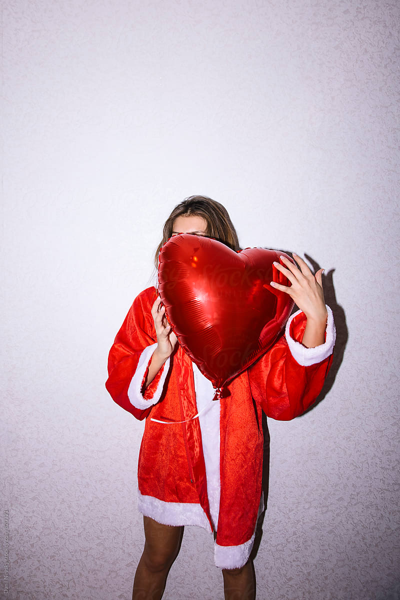 Young Woman In Santa Claus Costume Hiding Her Face With Red Balloon 