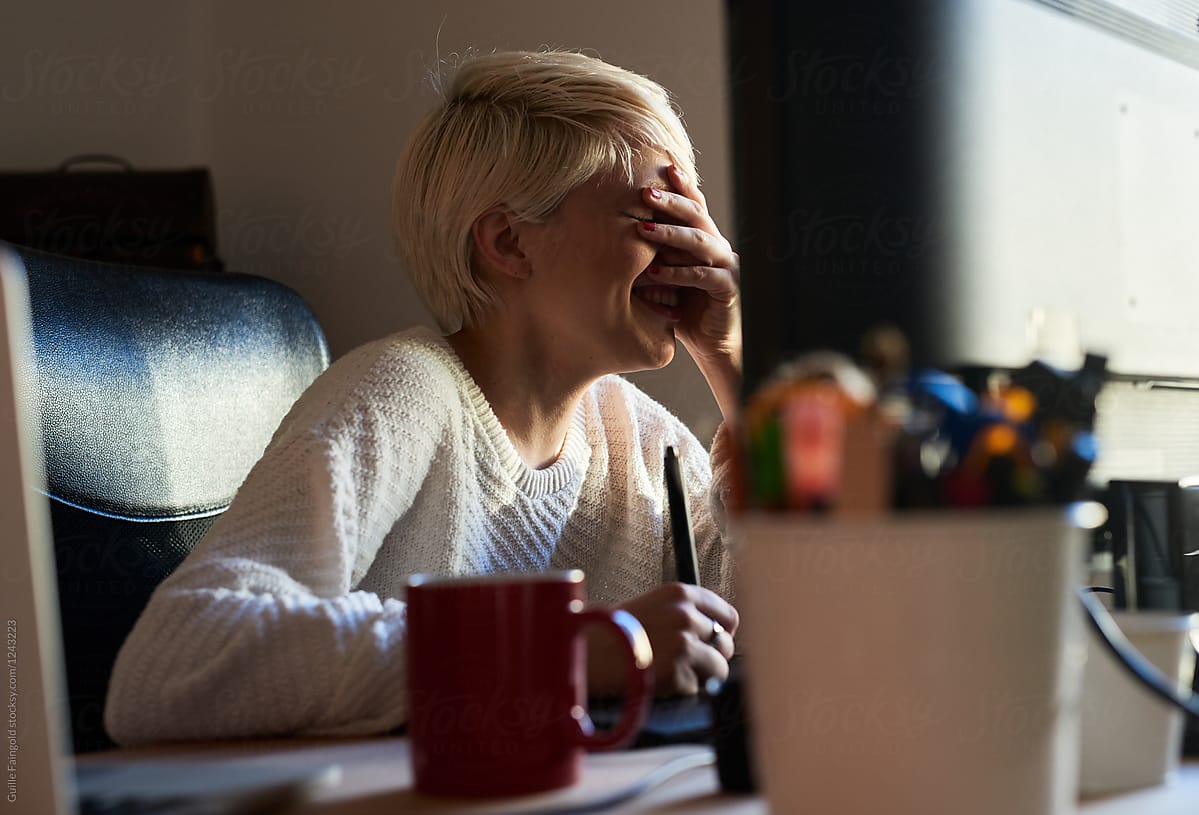 Smiling woman covering face with hand at office desk.