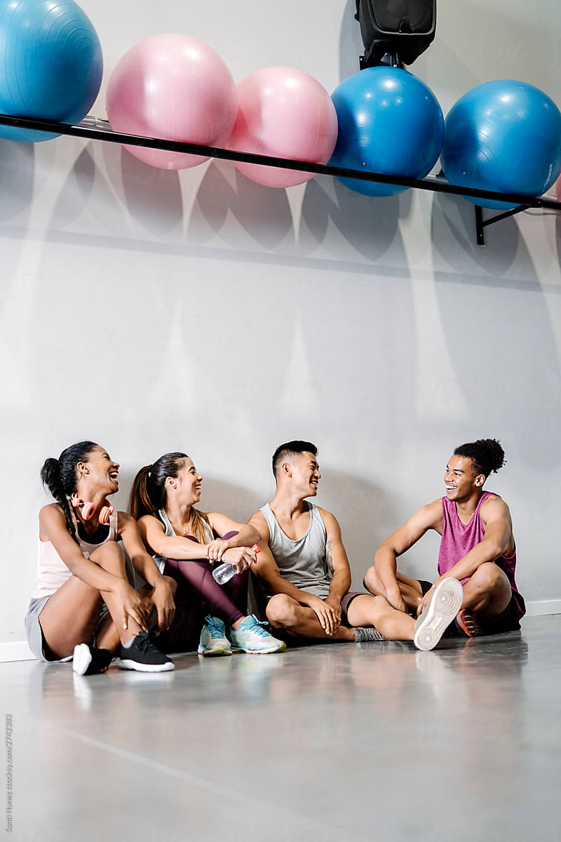Group of young sporty people sitting on the floor against white wall