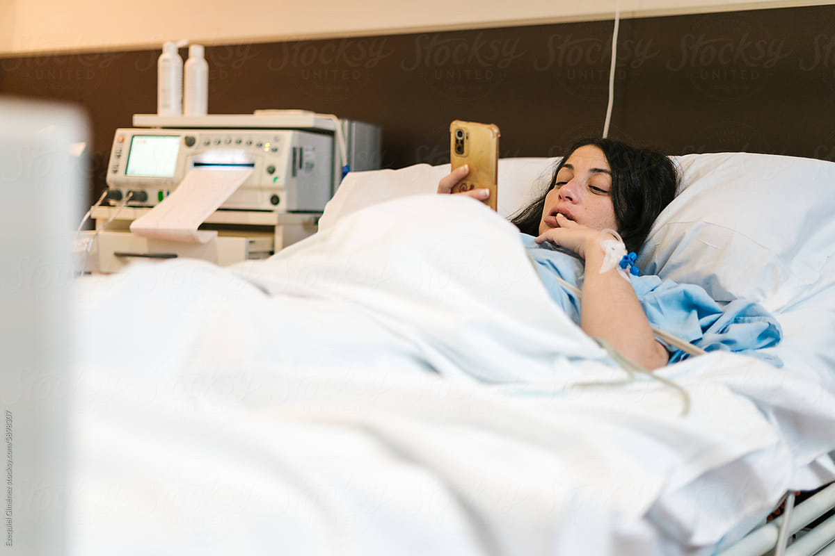 Pregnant female patient using smartphone while lying in hospital room