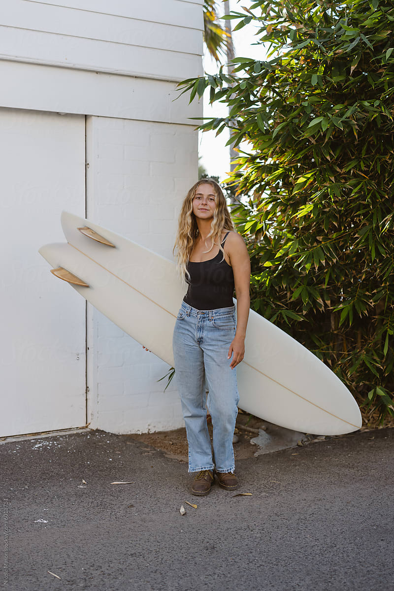 young woman in casual clothing holding surf board and smiling softly