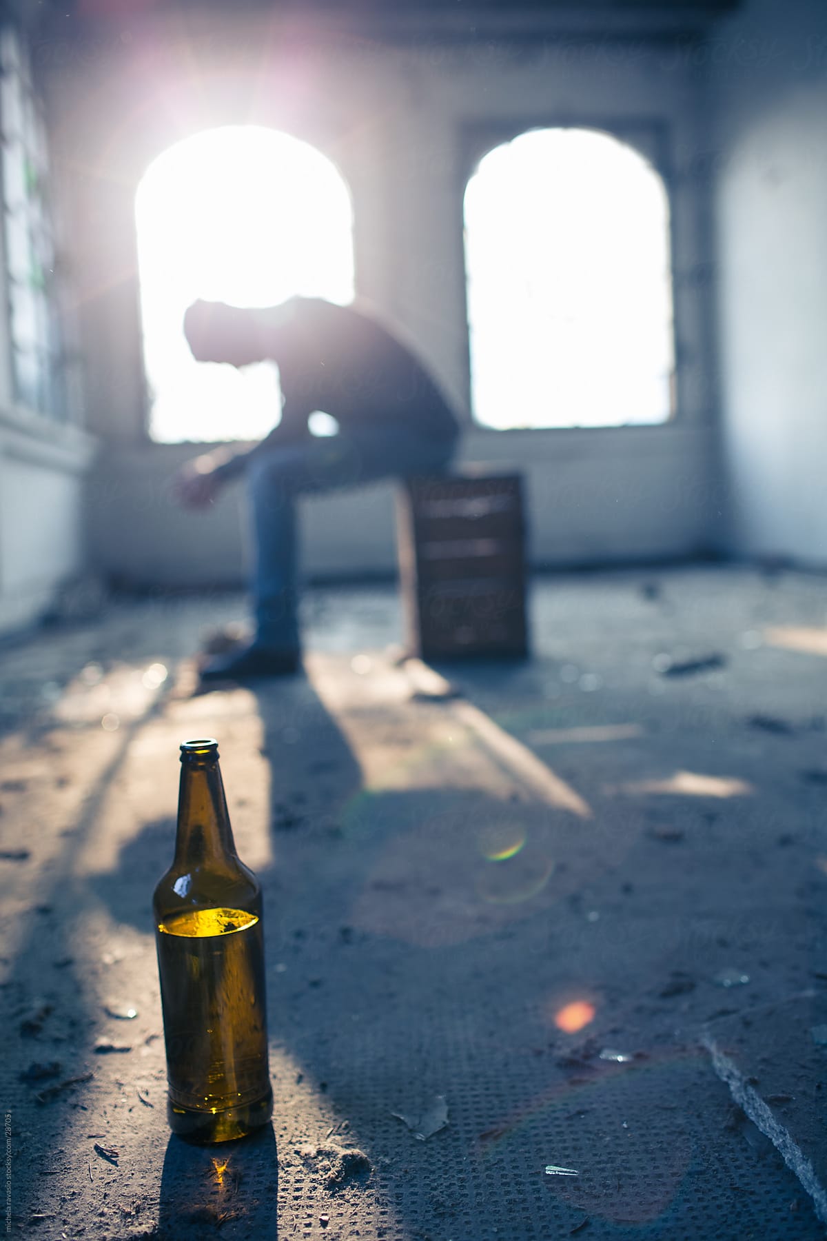 Depressed man sitting on a box with a bottle.