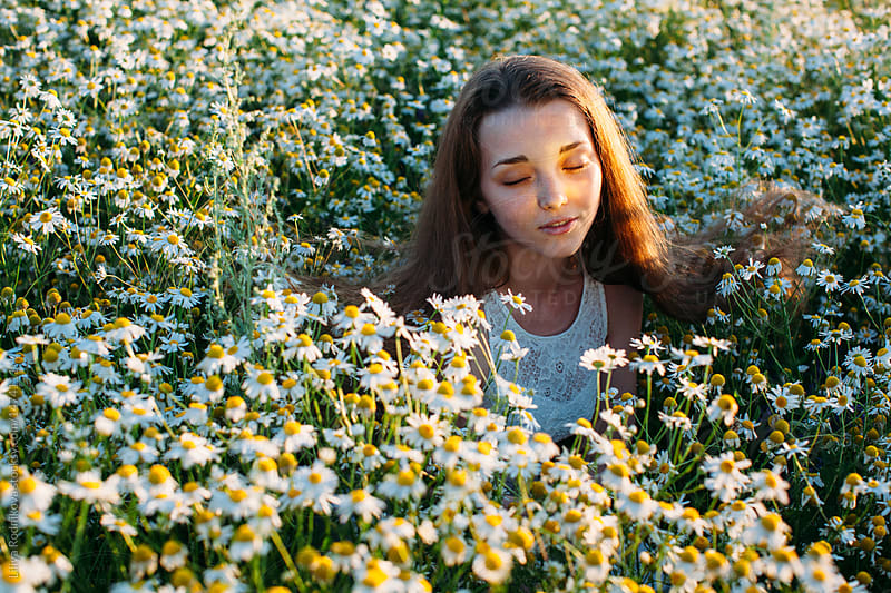 Emotional portrait of pretty young female in camomile field with sunbeam on her face