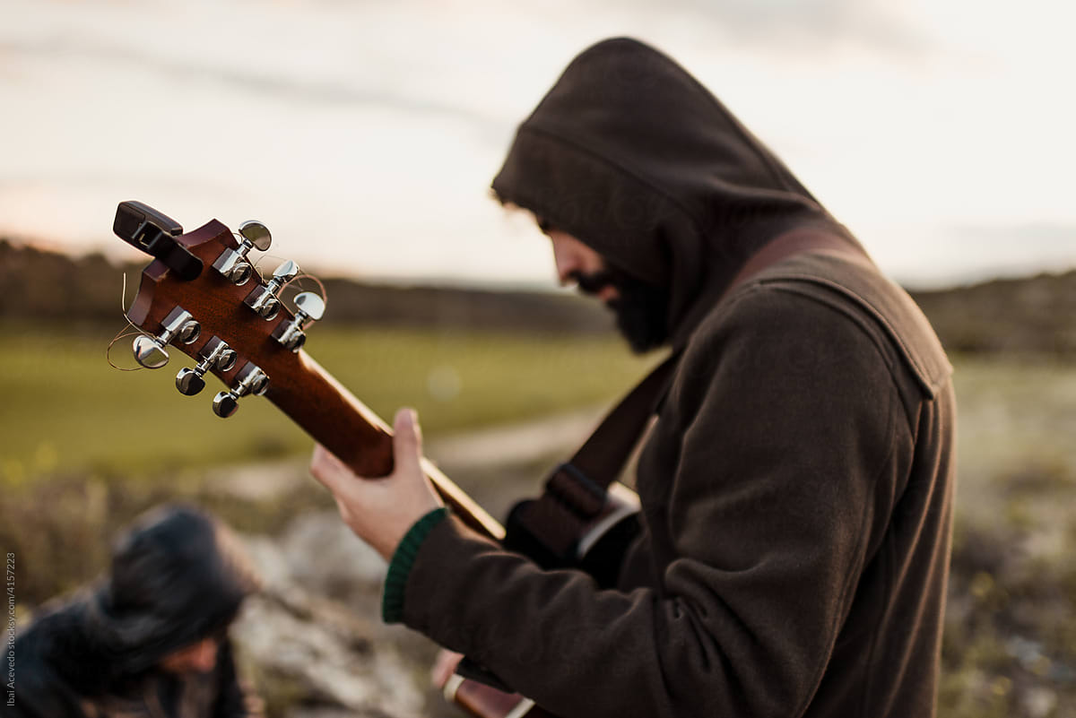 Musician with hood on playing guitar