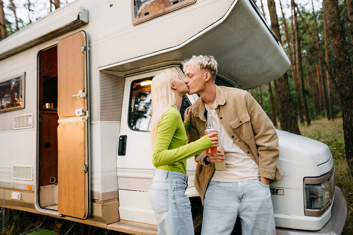 A man and a woman kiss standing near a van