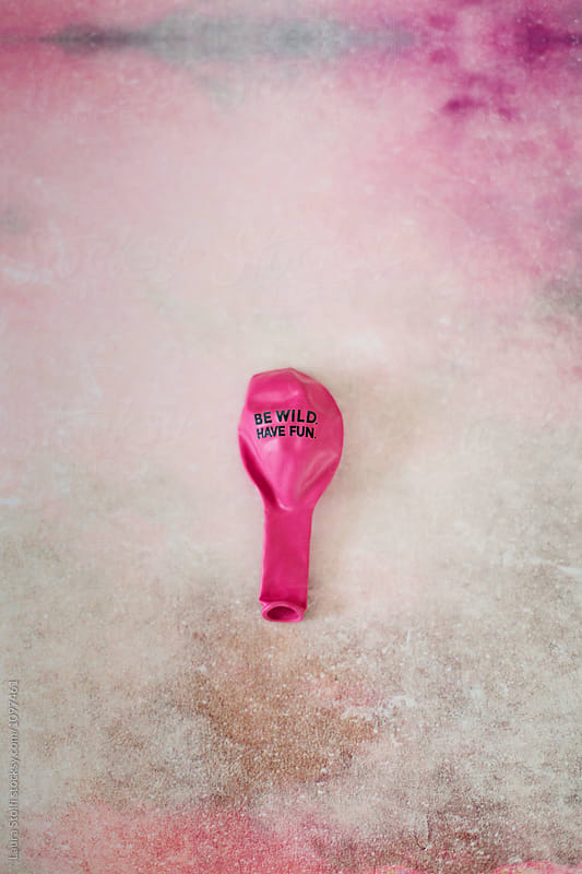 Still life of flat pink balloon and words Be wild, have fun printed on it