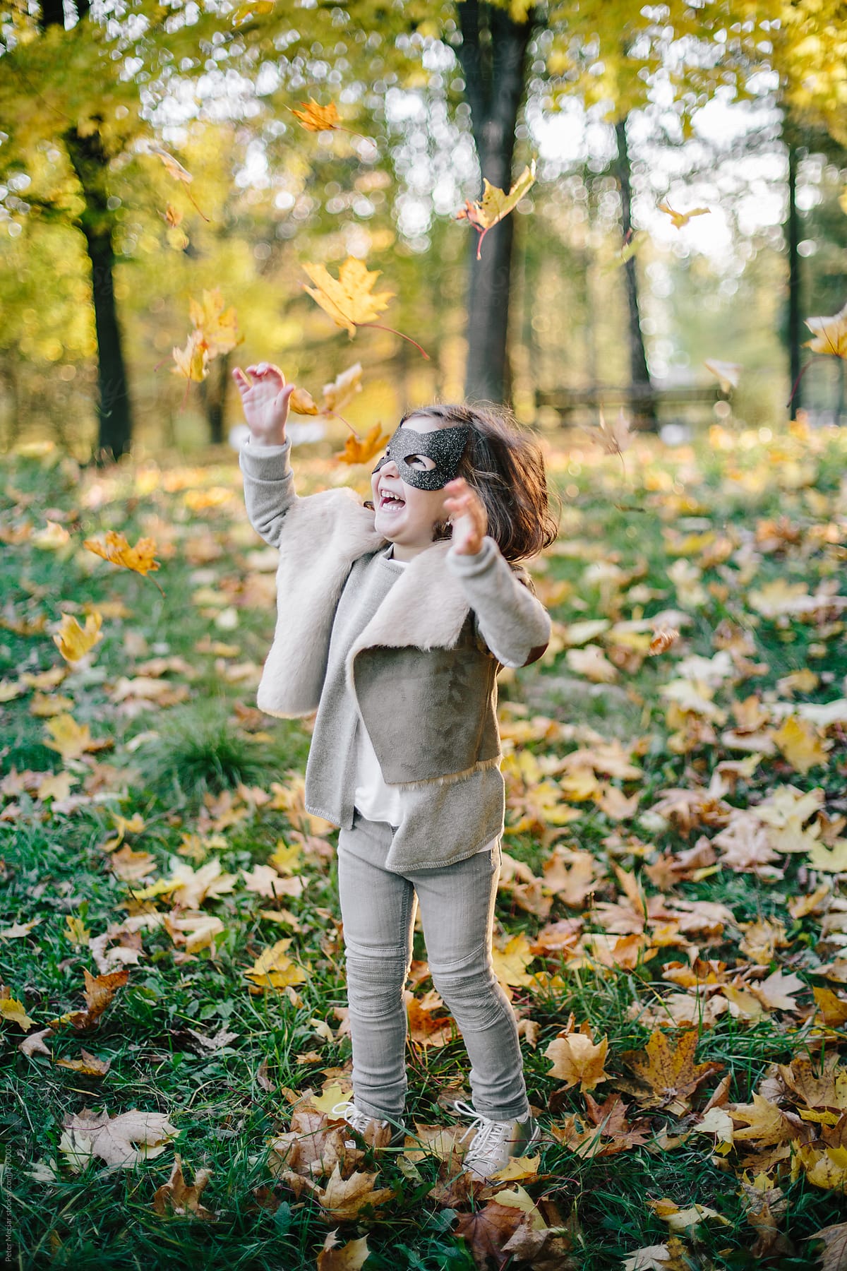 Little girl with a face mask is playing in autumn park and throw autumn leaves