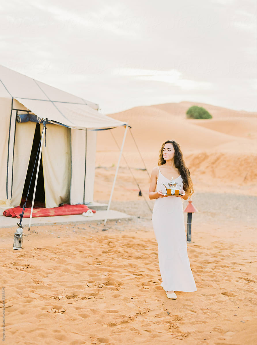 A portrait of a dark-haired woman serving moroccan mint tea in the desert camp