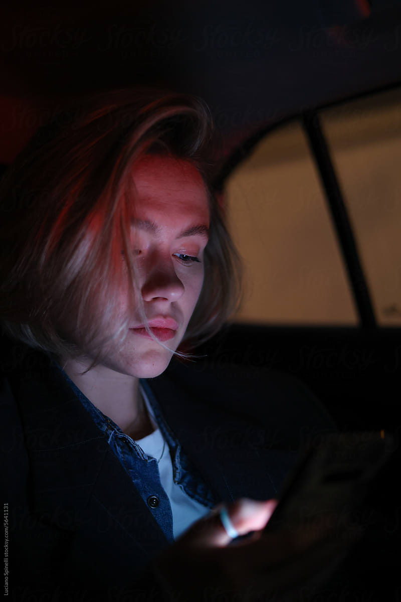 Blond young woman using social media on her mobile phone inside car