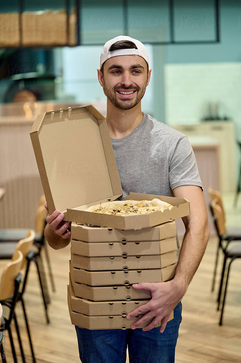 a young man is holding a stack of pizza boxes