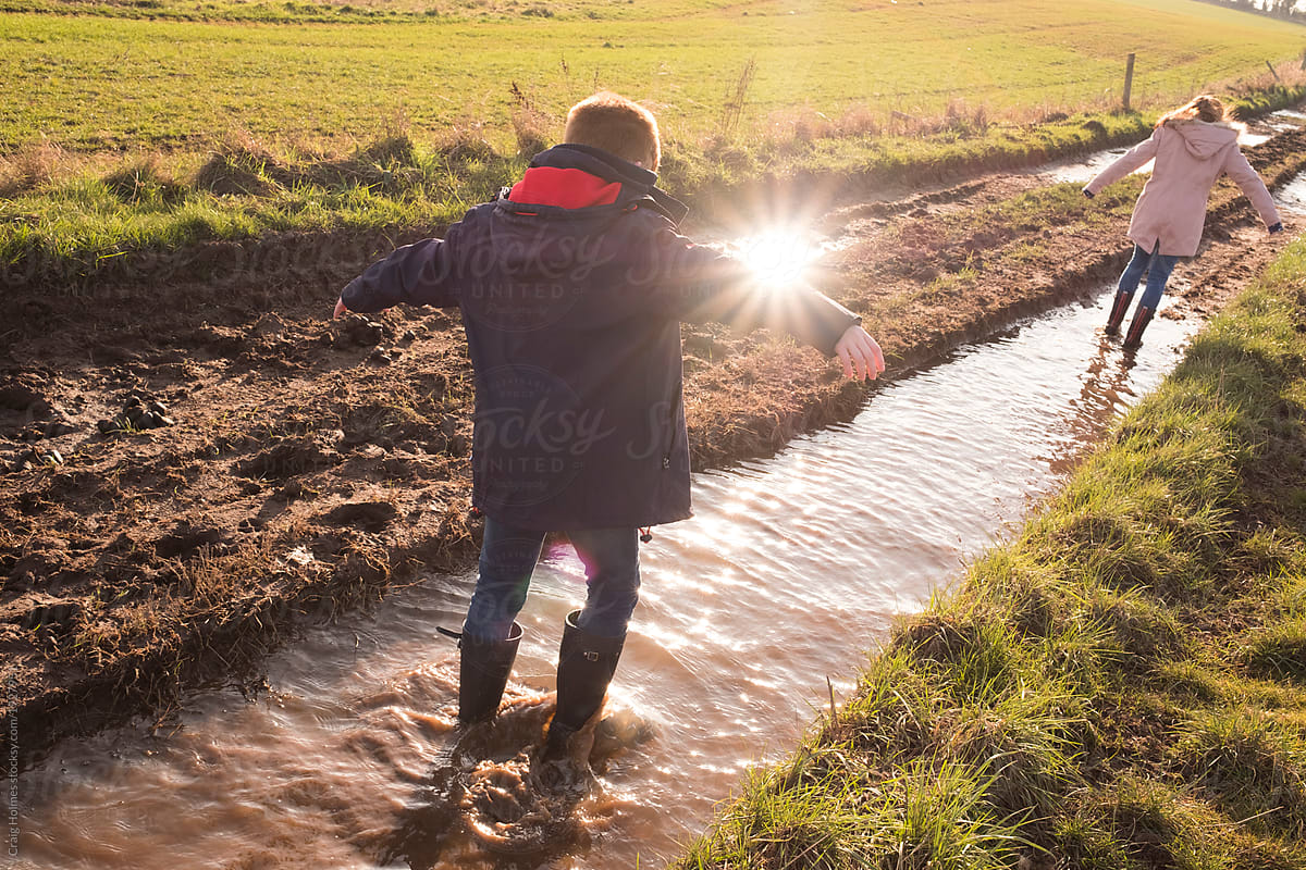 A teenage boy and girl splashing in puddles of mud on a country